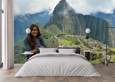 Attractive young Latina brunette woman with long hair sitting in the ruins of Machu Picchu and happy after arriving at one of the seven wonders of the world wearing sports clothes Wall mural