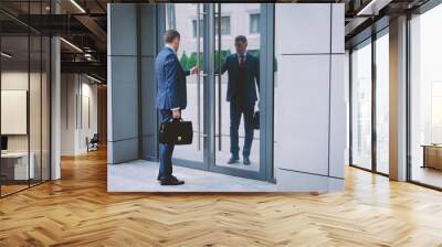 serious man in a suit with a briefcase hurries to a meeting in the business center. Businessman opens office door. Business life in the city. Wall mural