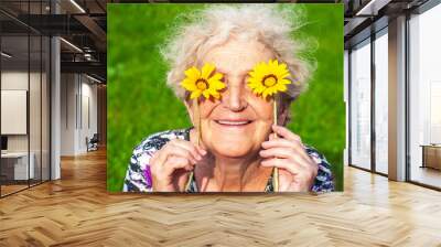 A cheerful grandmother looks at the flower look of yellow daisies. Women's health, skin care, eyesight, sunburn, healthy teeth, wrinkles in old age Wall mural