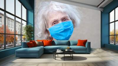 An elderly old woman in a protective respirator mask on her face is terrified holding her hands to her head. Elderly and coronovirus infection COVID-19. Retirement Health at Risk Wall mural