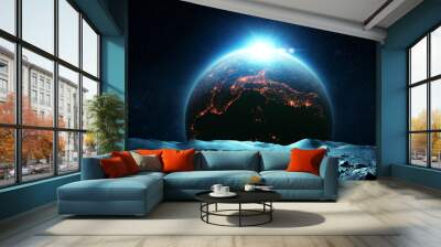 Astronaut man in a space suit and a lunar rover exploring the surface of the moon. Beautiful moon and planet Earth with night city lights and dawn rays. Amazing space wallpaper Wall mural