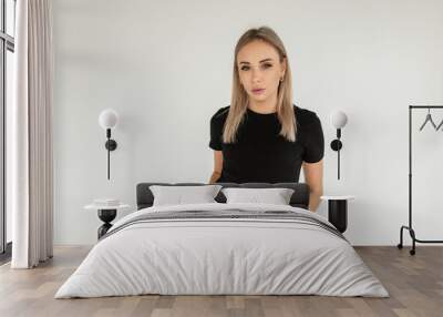 Beautiful fashionable young blonde woman in a black mockup t-shirt and black jeans stands in the studio on a white background and looks at the camera Wall mural