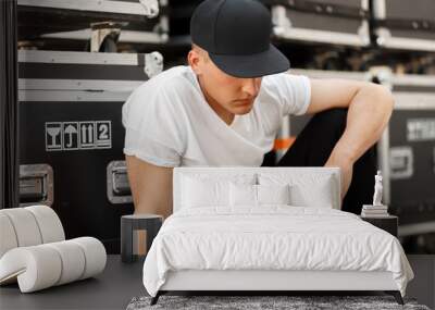 Fashion young man in a fashionable black cap with a stylish white t-shirt sitting near the boxes Wall mural