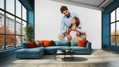 Happy beautiful fashion couple in the studio. Hipster handsome man and pretty redhead woman in casual elegant clothes sitting on white background Wall mural