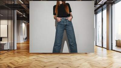 Stylish young pretty girl in trendy vintage clothes with black t-shirt, blue jeans and glasses in studio with hard light. Cool woman Wall mural