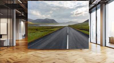 Deserted mountain road sloping down toward the sea in Iceland on a cloudy summer evening Wall mural