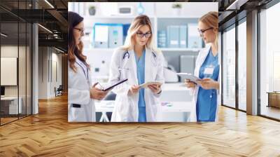 Team of three women doctors collaborates in a hospital office, reviewing a patient's medical chart Wall mural