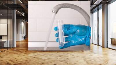 Analysis of tap water in the house, hand in blue glove draws water into a test tube from the tap for laboratory test, close-up Wall mural