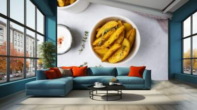 Baked potato wedges with sour cream sauce on a light background, top view. Rustic baked potatoes in the oven on a white plate with herbs. Wall mural