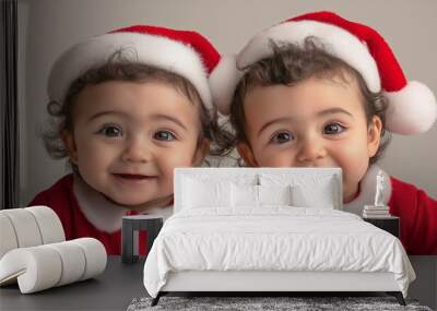 Photo of two one-year-old Hispanic twins against a light background, dressed in a Santa Claus costume, happy and smiling. Photo from above. Christmas concept. Advertising banner. Wall mural