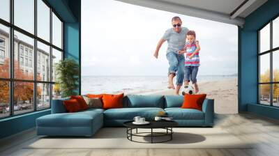 Father and son playing football on the beach at the day time. Wall mural