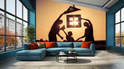 Happy family standing on the field at the sunset time. They build a house. Wall mural