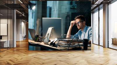 Casual tired office worker sitting at desk using computer and doing overtime project in lamplight.  Wall mural