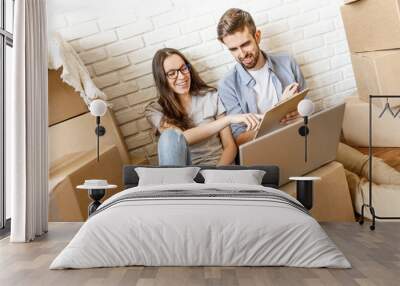 Cheerful man and woman making list on clipboard before relocating while sitting with laptop and boxes. Wall mural