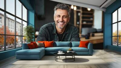 Middle-aged man with gray hair and beard smiling indoors in a modern and cozy living room setting during daytime Wall mural