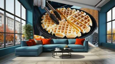 person taking waffles out of iron with tongs Wall mural