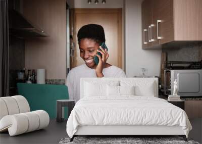 Smiling black woman talking on smartphone while using laptop Wall mural