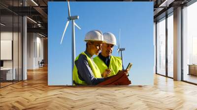 Two engineers using mobile phone while working in a wind turbine farm. Wall mural