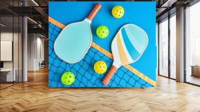 two paddles and four pickleball balls on top of a net on blue background Wall mural