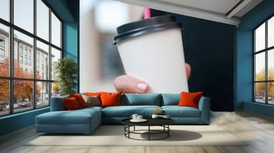 Paper coffee cup in woman's hand, city street in the background Wall mural