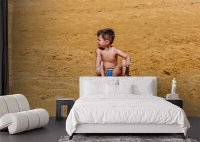 a four-year boy sits on the sand at the beach Wall mural