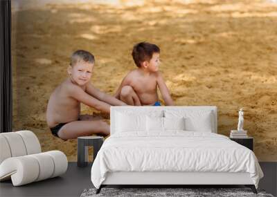 two tanned preschooler boys bury their feet in the sand on the beach in summer Wall mural