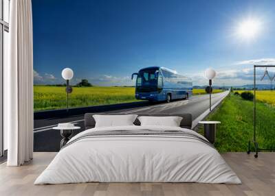 Blue bus driving on the asphalt road between the yellow flowering rapeseed fields under radiant sun in the rural landscape Wall mural