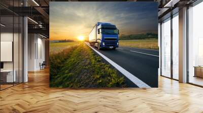 Blue truck arriving on the asphalt road in rural landscape at sunset Wall mural