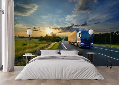 Blue truck driving on the asphalt road in rural landscape at sunset Wall mural