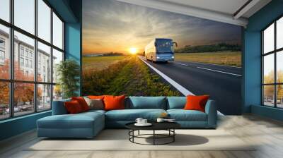 bus traveling on the asphalt road in rural landscape at sunset Wall mural