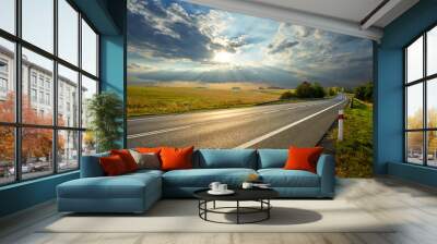 Empty asphalt road in rural landscape at sunset with dramatic clouds Wall mural