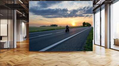 Motion blur motorcycle riding on asphalt road towards the horizon in rural landscape at sunset. Red car in the distance. Wall mural