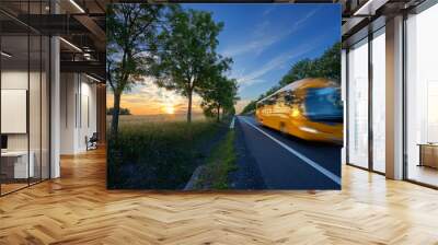 Motion blurred yellow bus traveling on the road in the avenue of trees in a rural landscape at sunset Wall mural