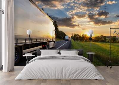 Two trucks driving on the asphalt road in rural landscape at sunset Wall mural