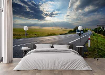 White bus traveling on the asphalt road in rural landscape at sunset with dramatic clouds Wall mural