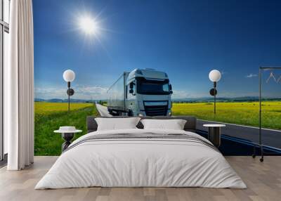 white truck driving on the asphalt road between the yellow flowering rapeseed fields under radiant s Wall mural