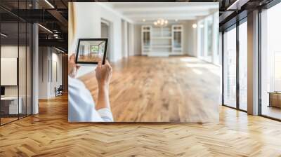 A person examines an empty interior space using a tablet to capture its design potential and lighting features during the day Wall mural