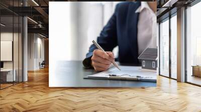 A professional signing a document with a model house, representing real estate investment and property management. Wall mural