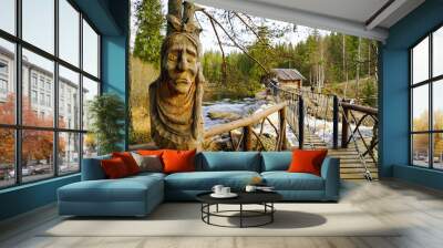 Carved wooden sculpture of an old woman near the pedestrian suspension bridge over a waterfall on the river tokhmayoki. Wall mural