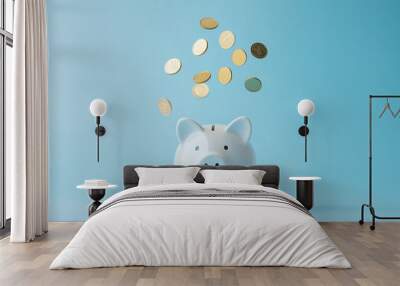 White piggy bank catching gold coins on a blue backdrop. Wealth accumulation and financial security concept. Wall mural