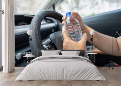 Asian woman driver holding bottle for drink water while driving a car. Plastic hot water bottle cause fire. Wall mural