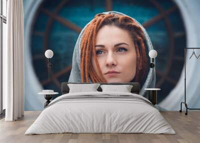 Portrait of a girl with dreadlocks of red color in a white sweatshirt with a hood on the background of a large round window Wall mural