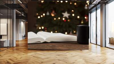 Open Bible book on a wooden table. A cup of coffee. Against the background of the Christmas tree Wall mural