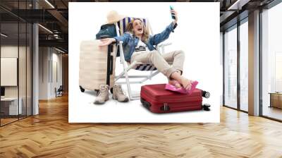 Happy joyful tourist woman in travel attire, on deck chair with trolley suitcases, make selfie with mobile phone. Summer beach holiday, flight and vacation travel booking. Travel influencer lifestyle Wall mural