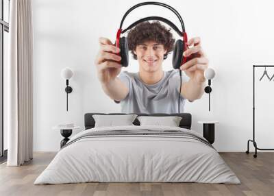 Young handsome smiling man, holding headphones in his hand and showing them to the camera before putting them on to listen to music or play video games, isolated against a white background Wall mural