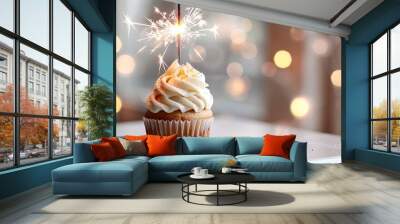 Festive cupcake topped with a sparkler on a white table, set against a background of blurred golden lights for celebratory occasions and special moments. Wall mural