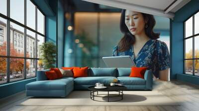 Portrait of a confident Asian businesswoman in stylish attire, using tablet in modern multicultural office, focused on financial and marketing strategy projects Wall mural