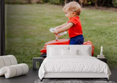 Baby girl riding toy car in garden Wall mural