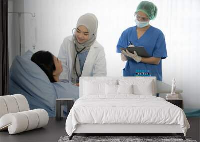 Asian female doctor wearing protective gears examination and treating patient in a hospital room Wall mural