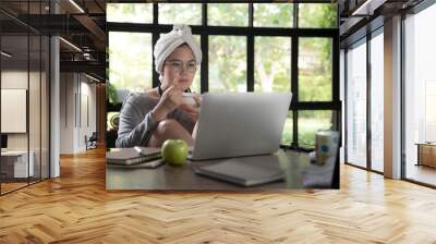 Asian young woman in casual clothing using laptop and smiling while working from home. Wall mural